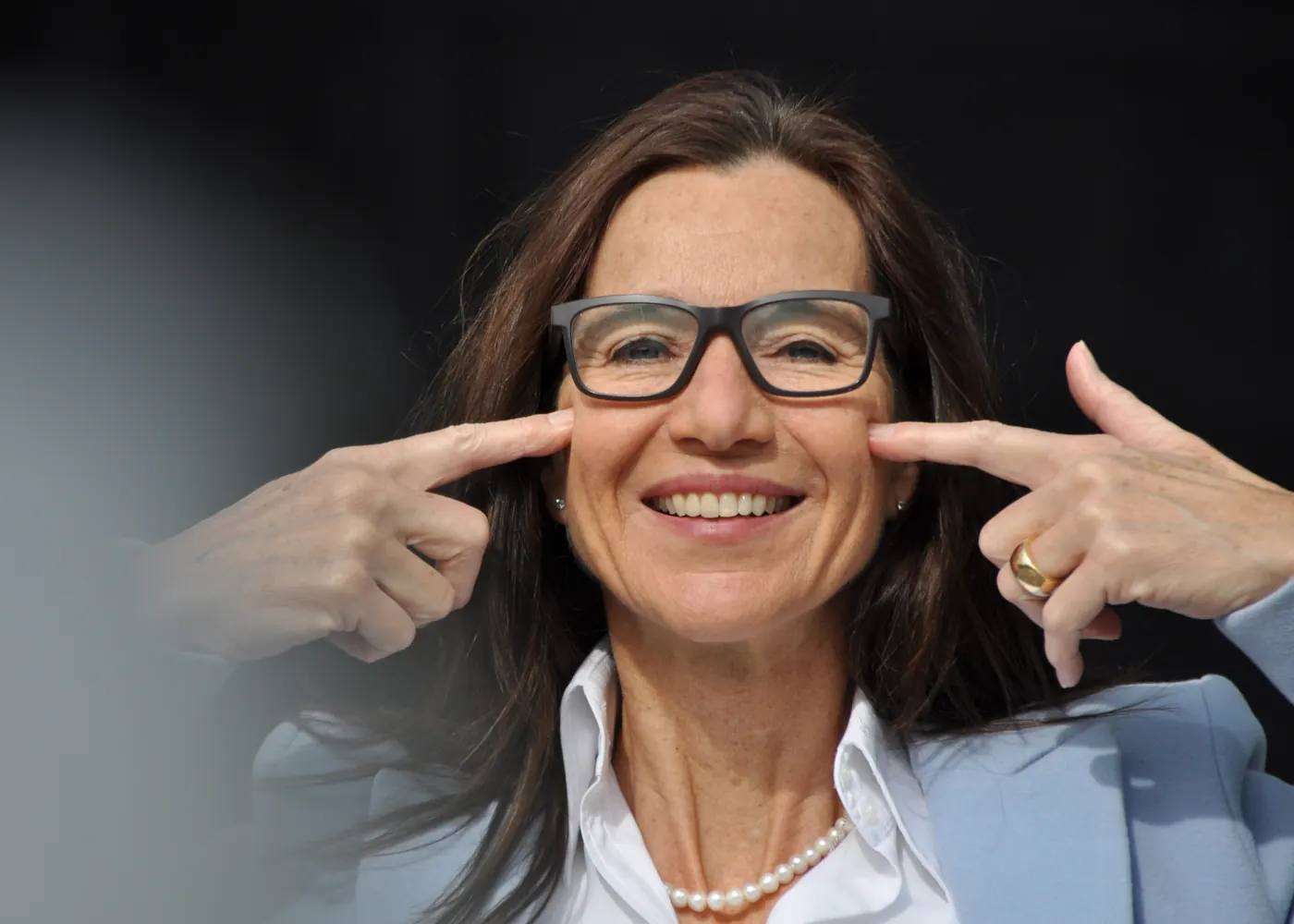 Delia Dittrich zeigt mit beiden Zeigefingern auf ihr Lächeln